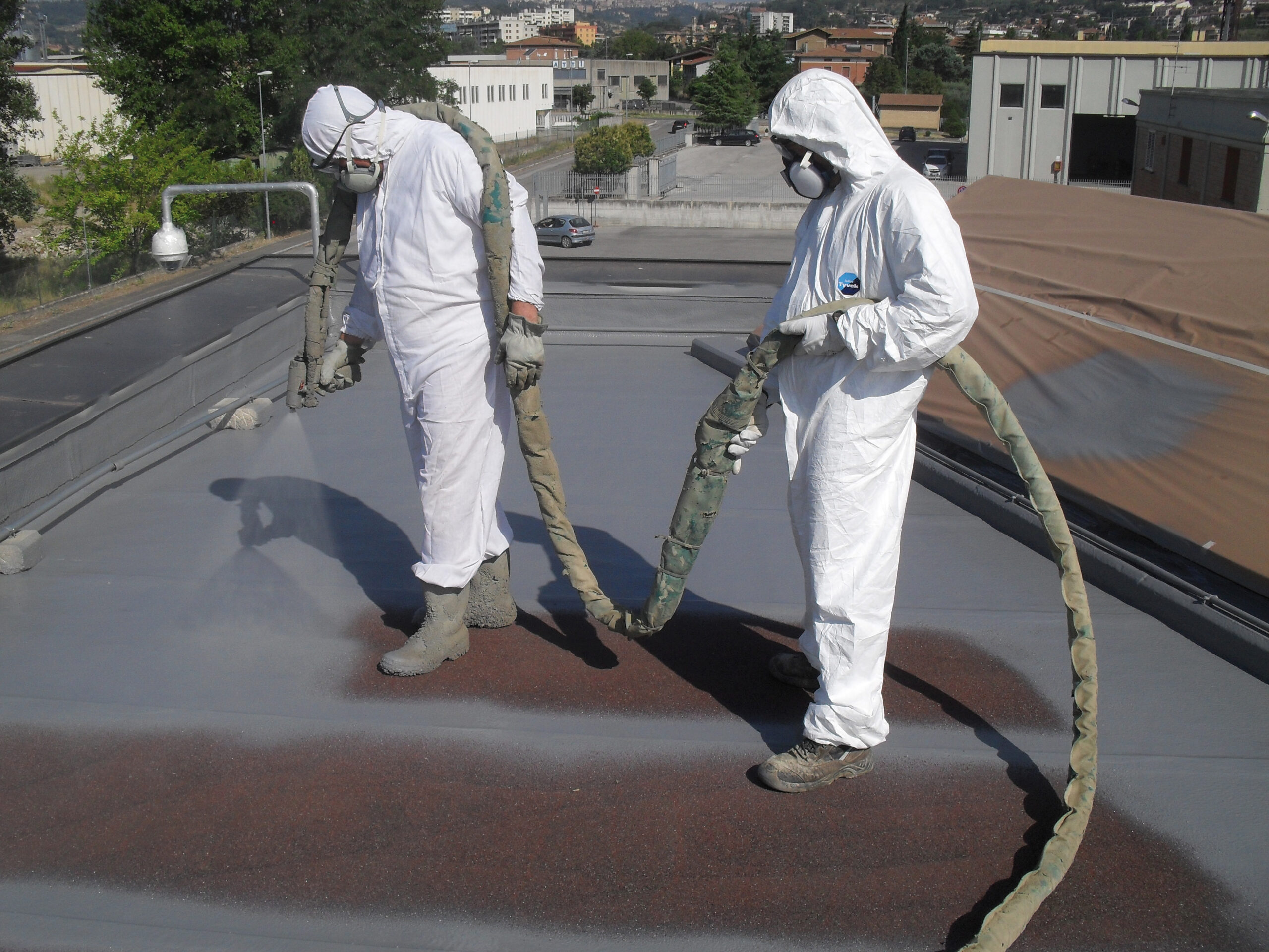 Two applicators in protective suits spraying a polyurea roof membrane